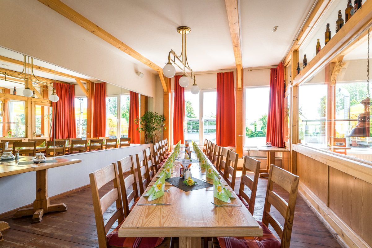 A long dining table with chairs, wooden beams, and large windows with red curtains.