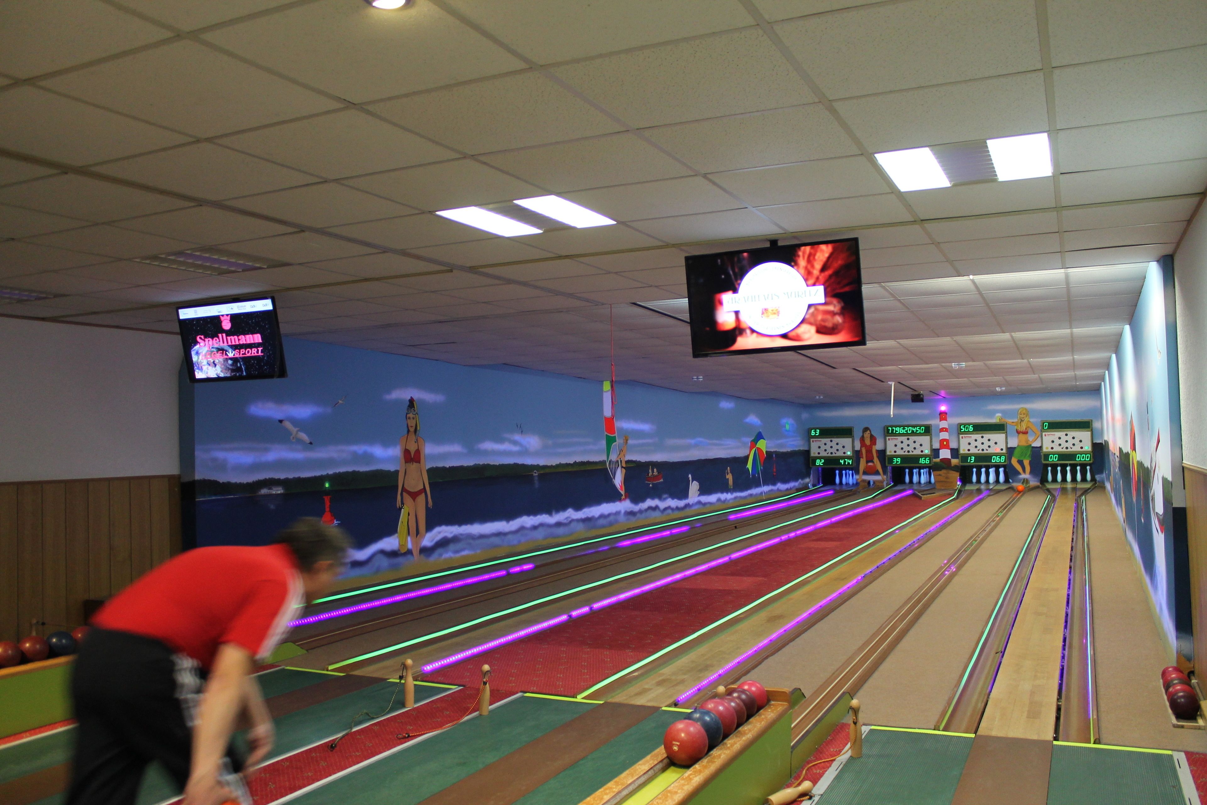 Eine Kegelbahn mit mehreren Bahnen, einem großen Bildschirm, der ein Bowling-Spiel zeigt, und einer Person, die kegelt.