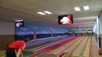 Eine Kegelbahn mit mehreren Bahnen, einem großen Bildschirm, der ein Bowling-Spiel zeigt, und einer Person, die kegelt.
