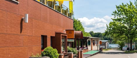 Un edificio con fachada de ladrillo, zona de estar al aire libre con sombrillas amarillas y un letrero visible que dice 'Drahaus Mürtz'.