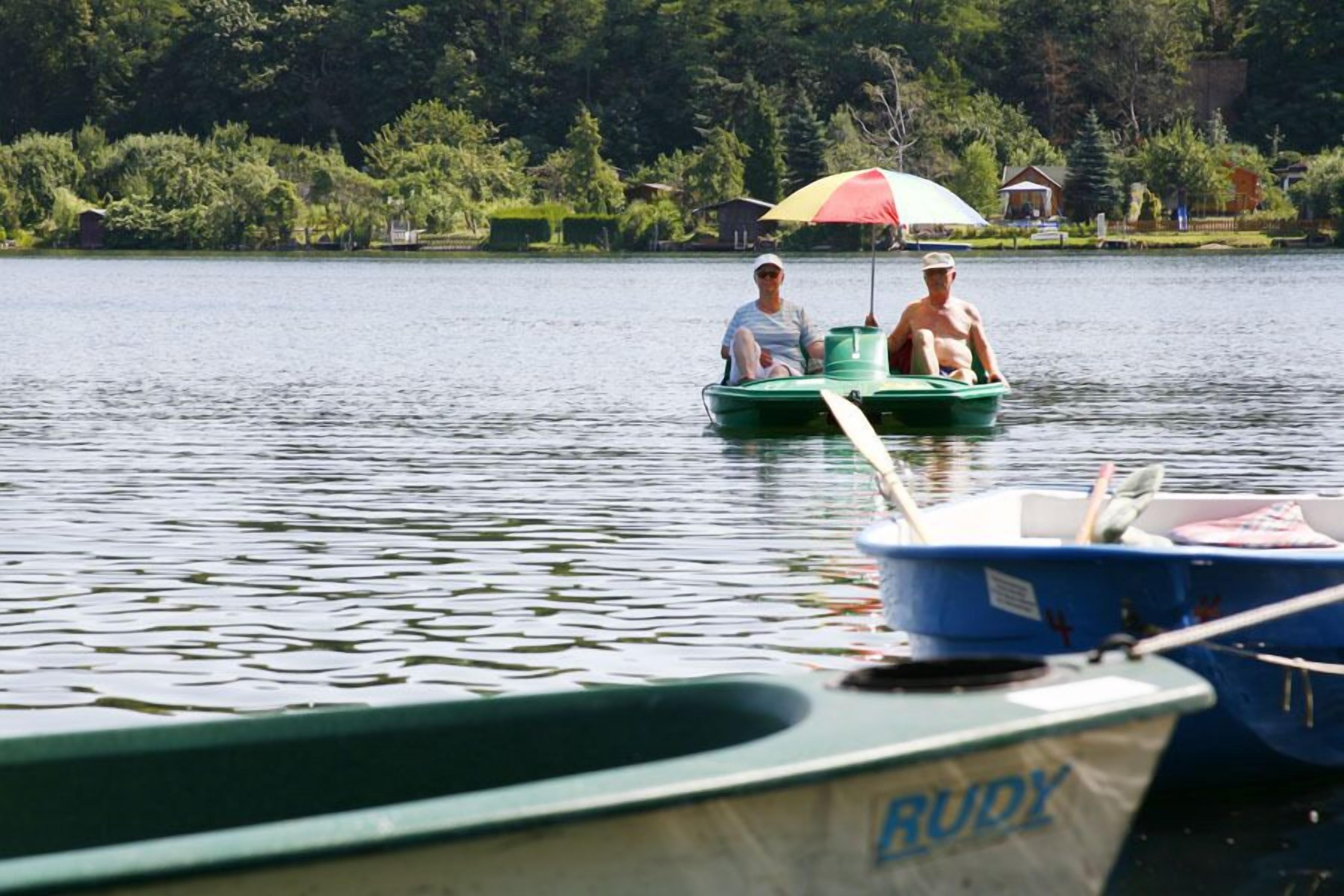 A calm lake with two people in a green boat and a blue boat docked nearby.