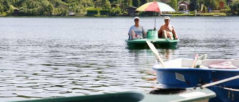 A calm lake with two people in a green boat and a blue boat docked nearby.