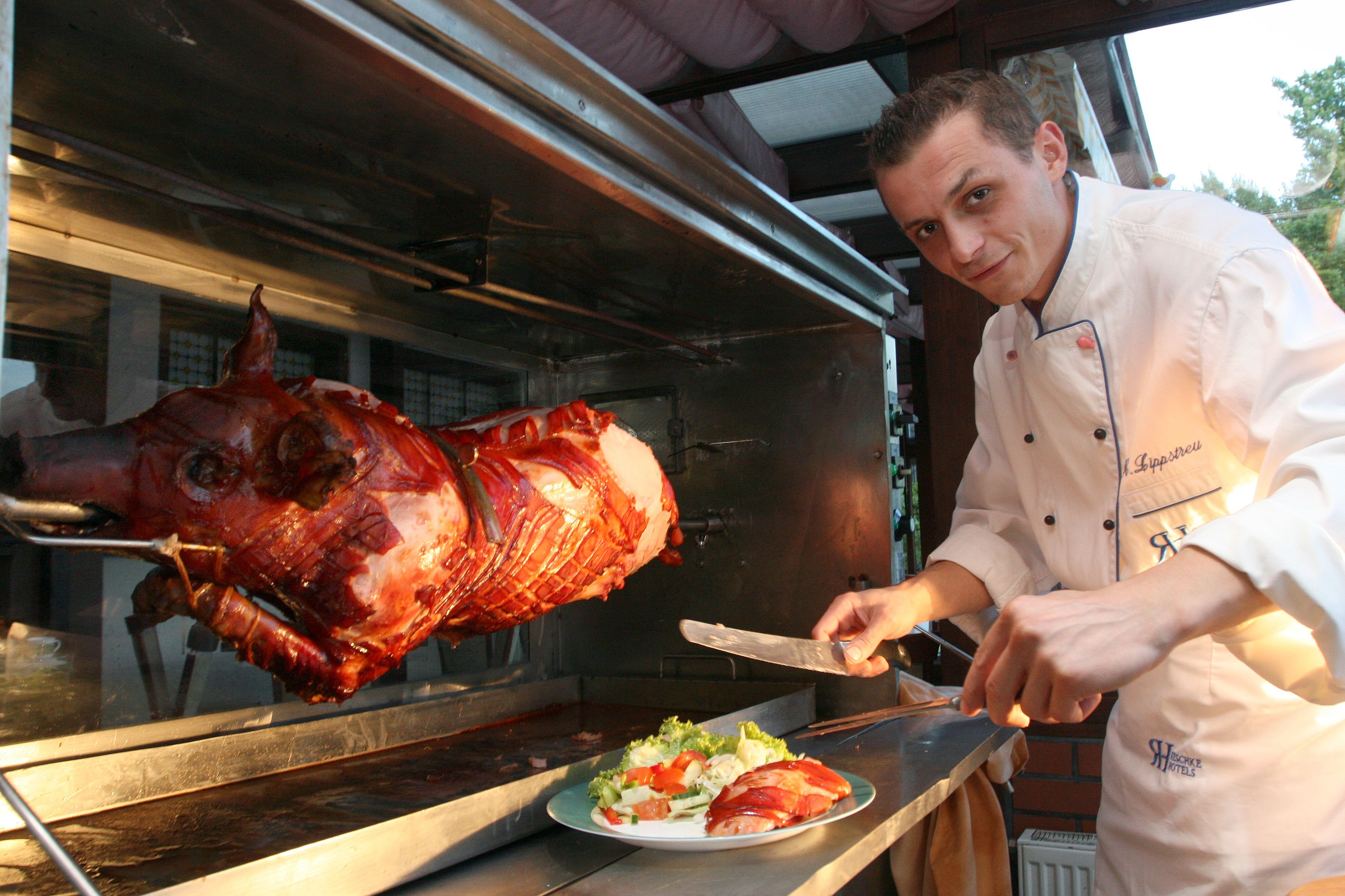 A chef carving a large roasted pig on a spit in a commercial kitchen.