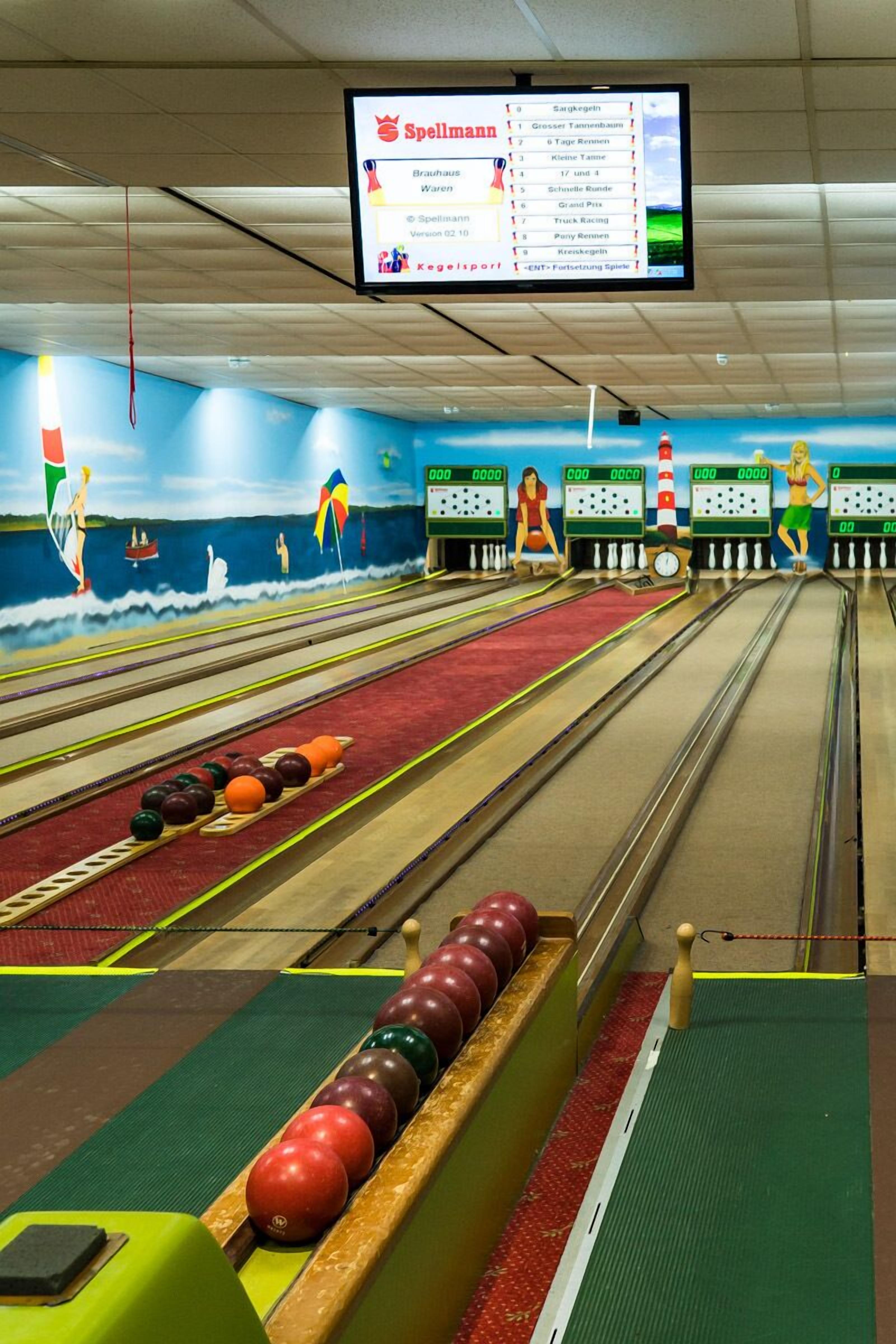 A bowling alley with multiple lanes, a scoreboard, and a mural of beach scenes.