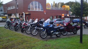 Una fila de motocicletas estacionadas frente a un edificio con un ventanal arqueado grande y un letrero que dice "BRAHMS".
