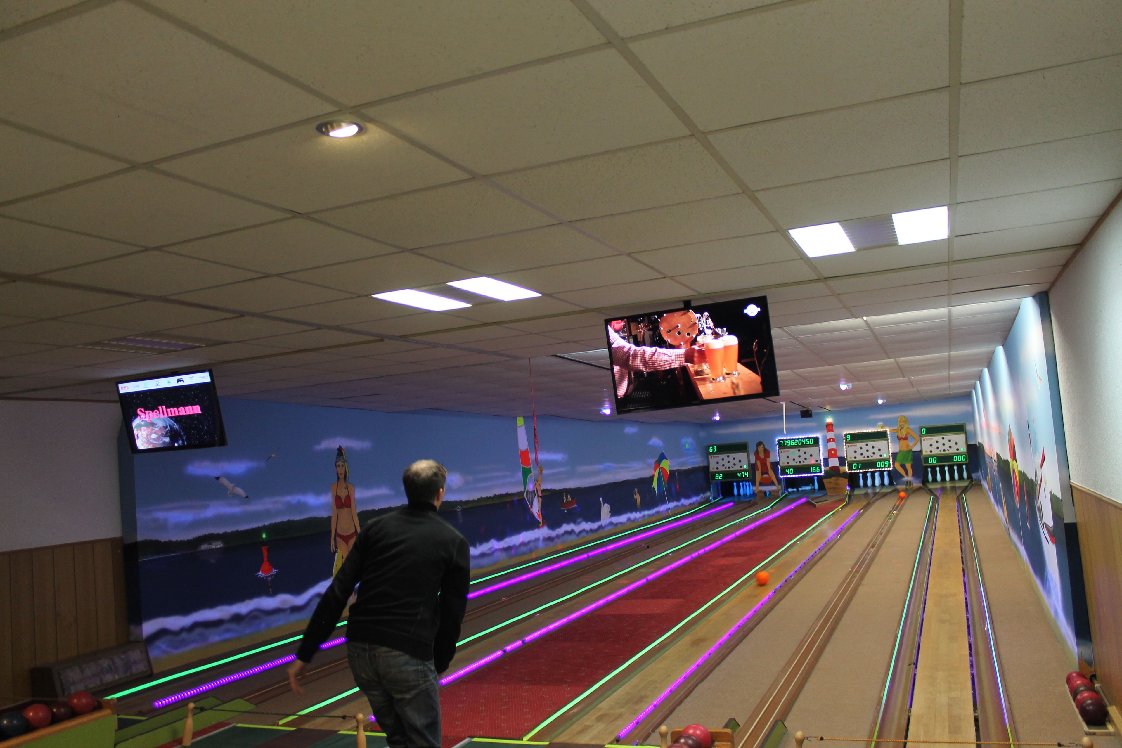 A bowling alley with multiple lanes, a large screen displaying a bowling game, and a mural on the wall.
