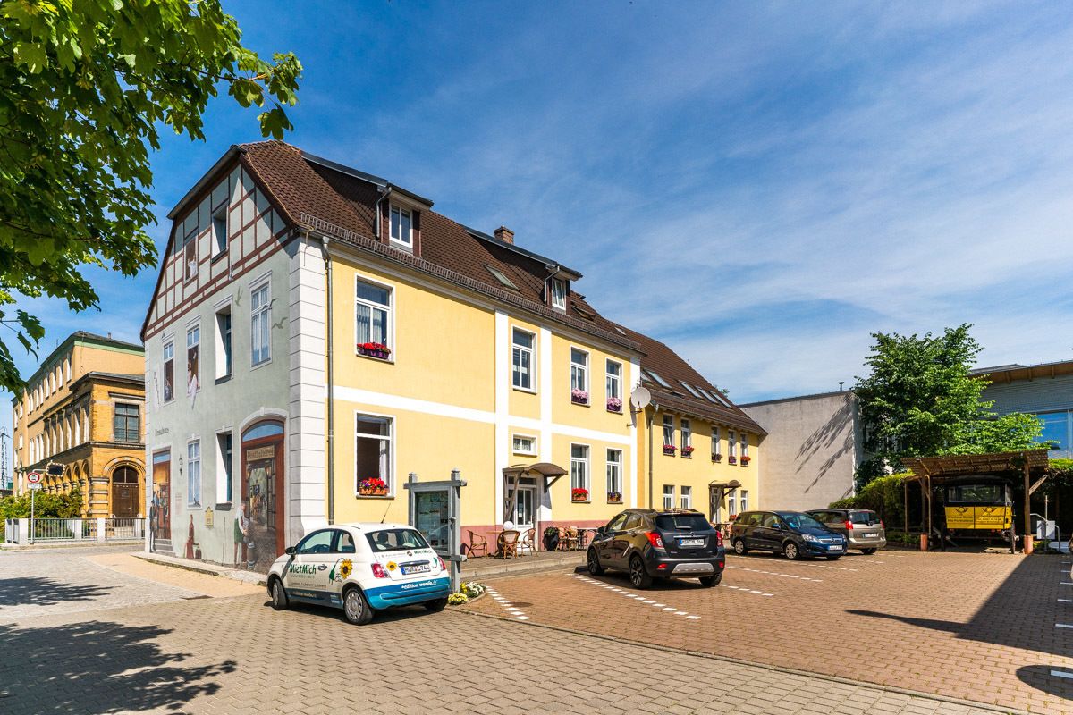 A yellow building with a traditional European architectural style, featuring a large entrance and a car parked in front.