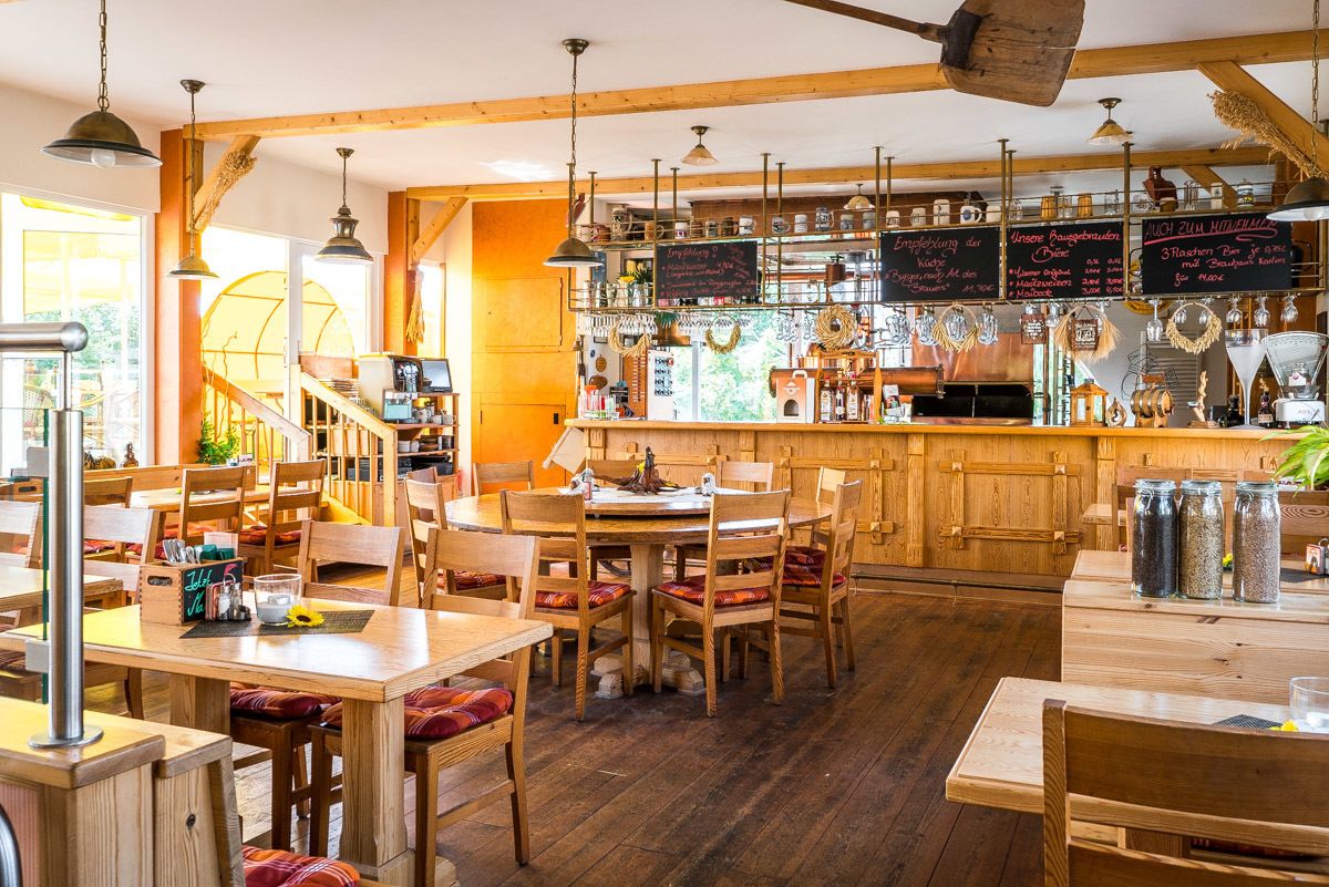 Un intérieur rustique en bois, avec un coin bar, des tables et des chaises en bois, et un escalier menant à un niveau supérieur.