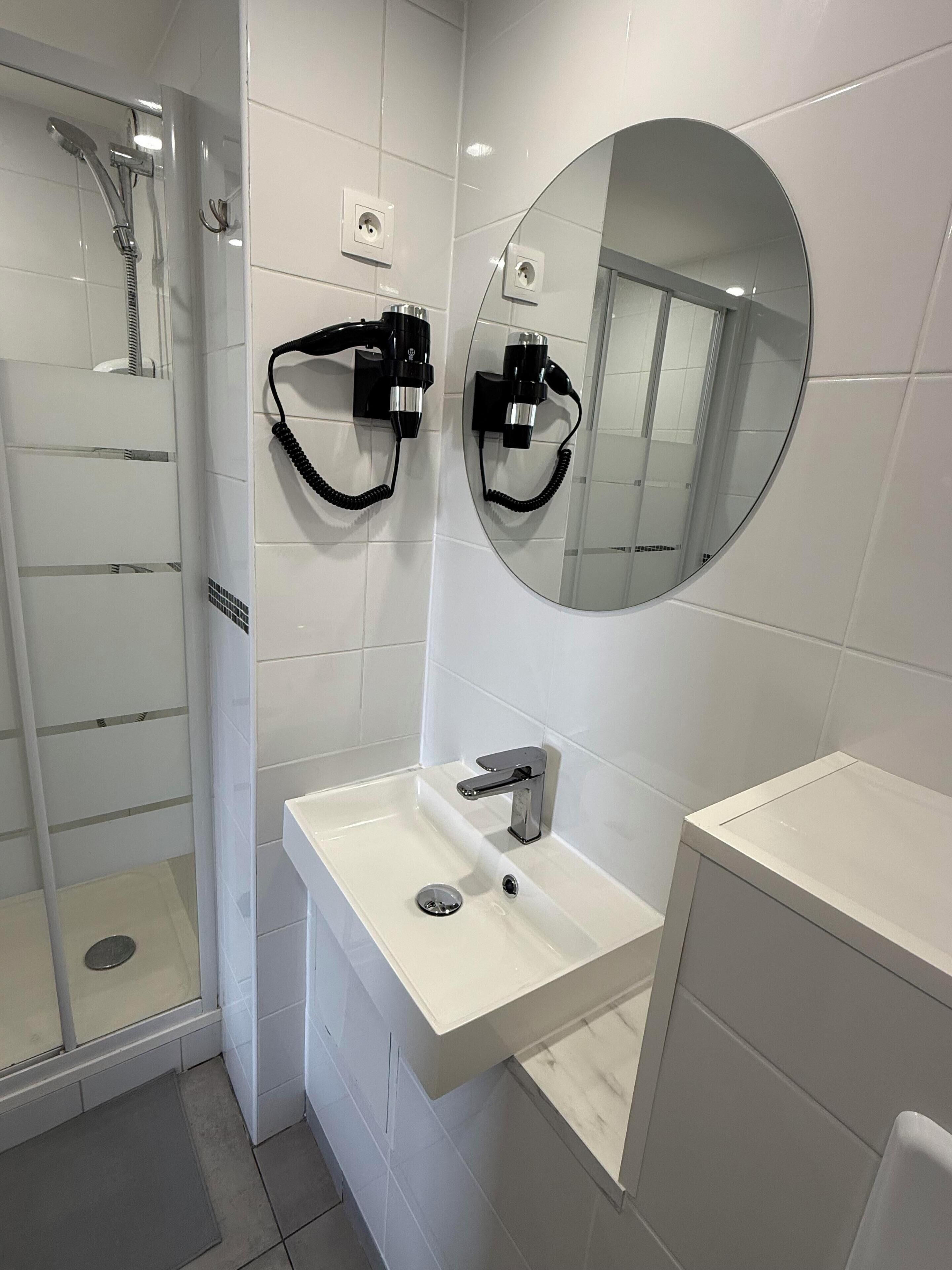 A modern bathroom with a glass shower enclosure, a white sink with a chrome faucet, and a round mirror above the sink.