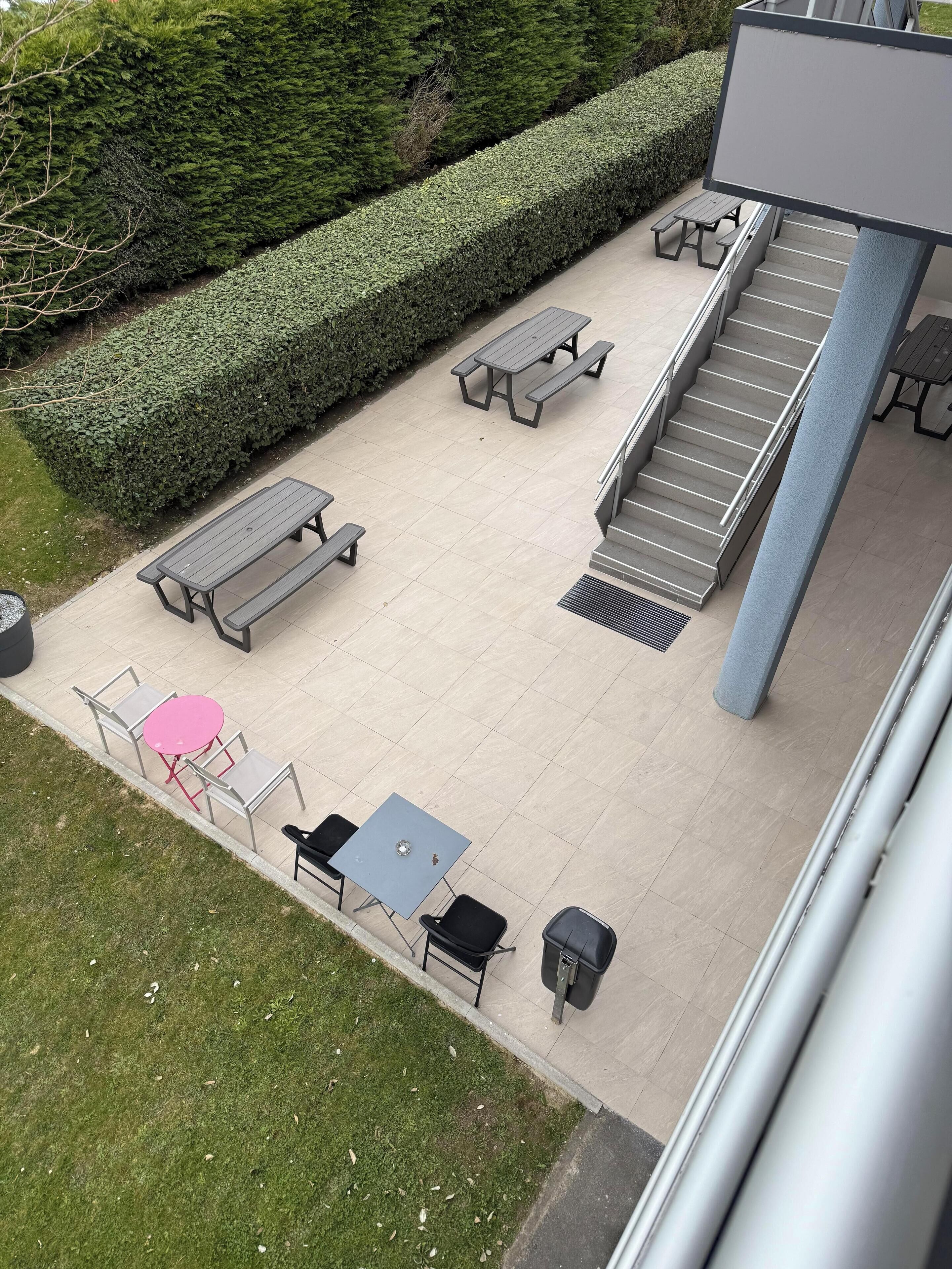 Un espace extérieur aménagé en terrasse, avec des tables de pique-nique, des chaises et une petite table recouverte d’une nappe rose.