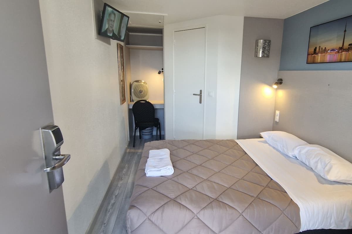 Habitación de hotel con cama, una silla, un escritorio y un cuadro de un paisaje urbano en la pared.