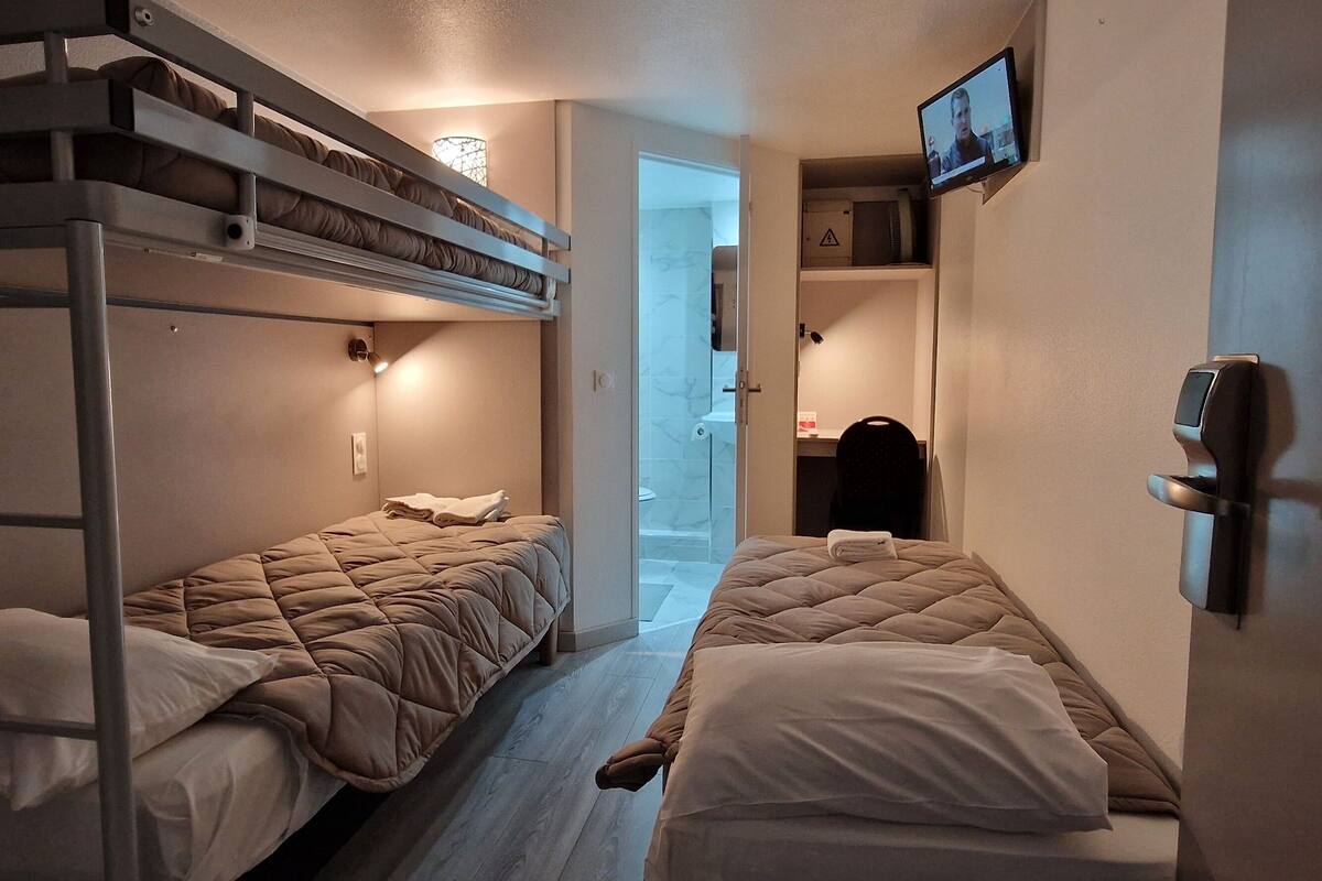 Una habitación con literas, una mesita de noche, un televisor montado en la pared y una puerta que da a otra habitación.
