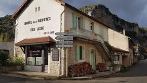 En bygning med et skilt, der viser 'HOTEL DES GROTTES TER ASSE PISCINE' og skilte med vejvisning til nærliggende steder.