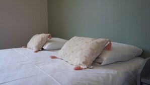 En seng med hvide sengetæpper og dekorative puder med kvaster.
