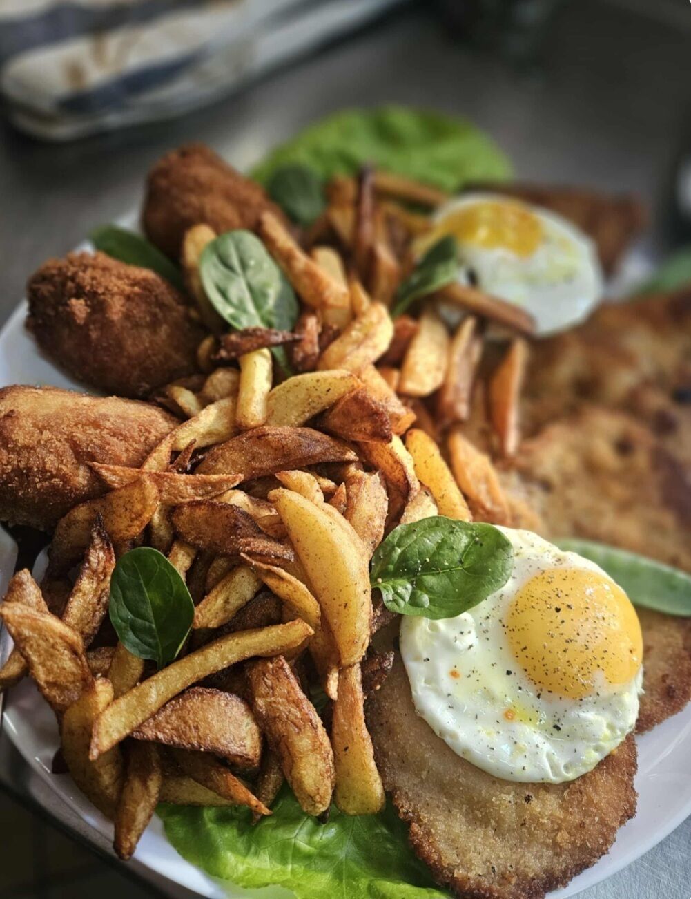 Un piatto con pollo fritto, patatine fritte, un uovo fritto e una fetta di pane.