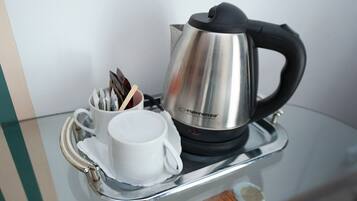 Una tetera eléctrica de acero inoxidable con asa negra y una taza blanca con una bolsita de té dentro, sobre una bandeja reflectante.