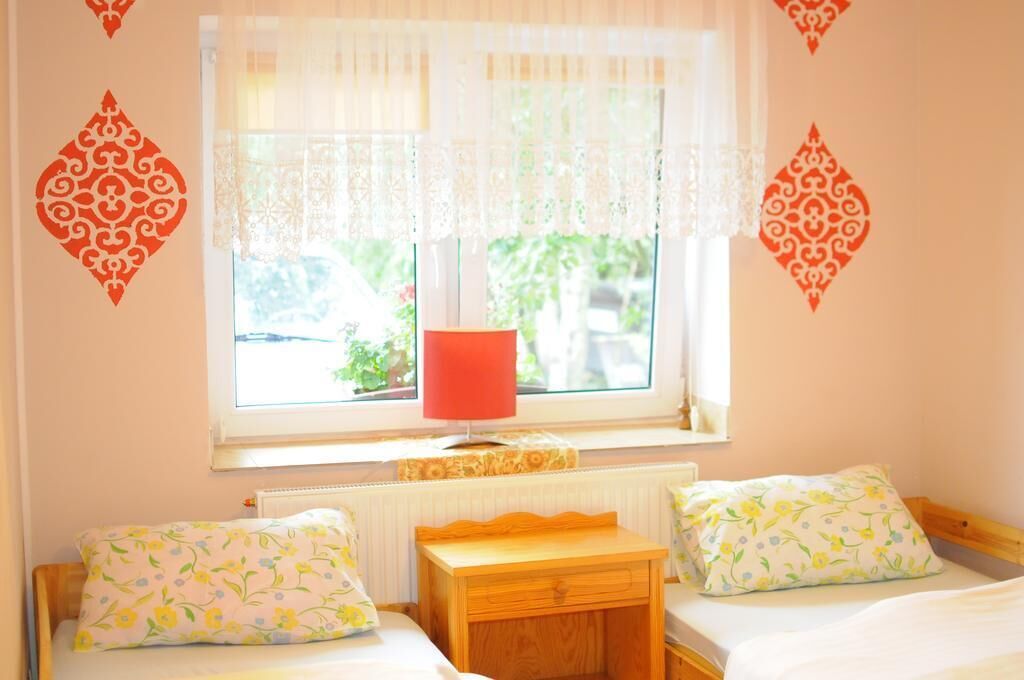 A bedroom with two beds, a window with lace curtains, a red lamp, and decorative wall stickers.
