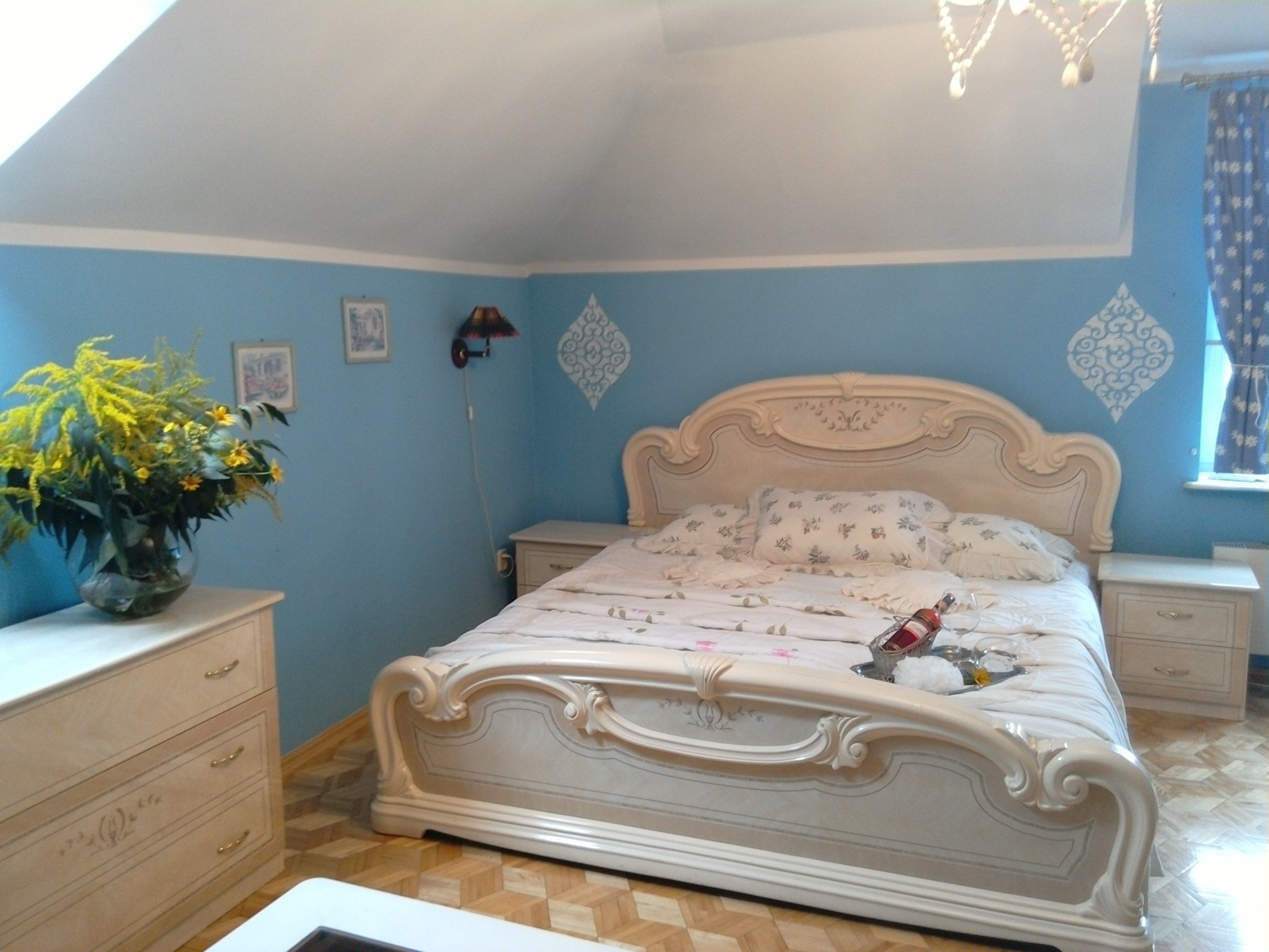 Un dormitorio con cama, cómoda, mesita de noche, lámpara y ventana con cortinas.