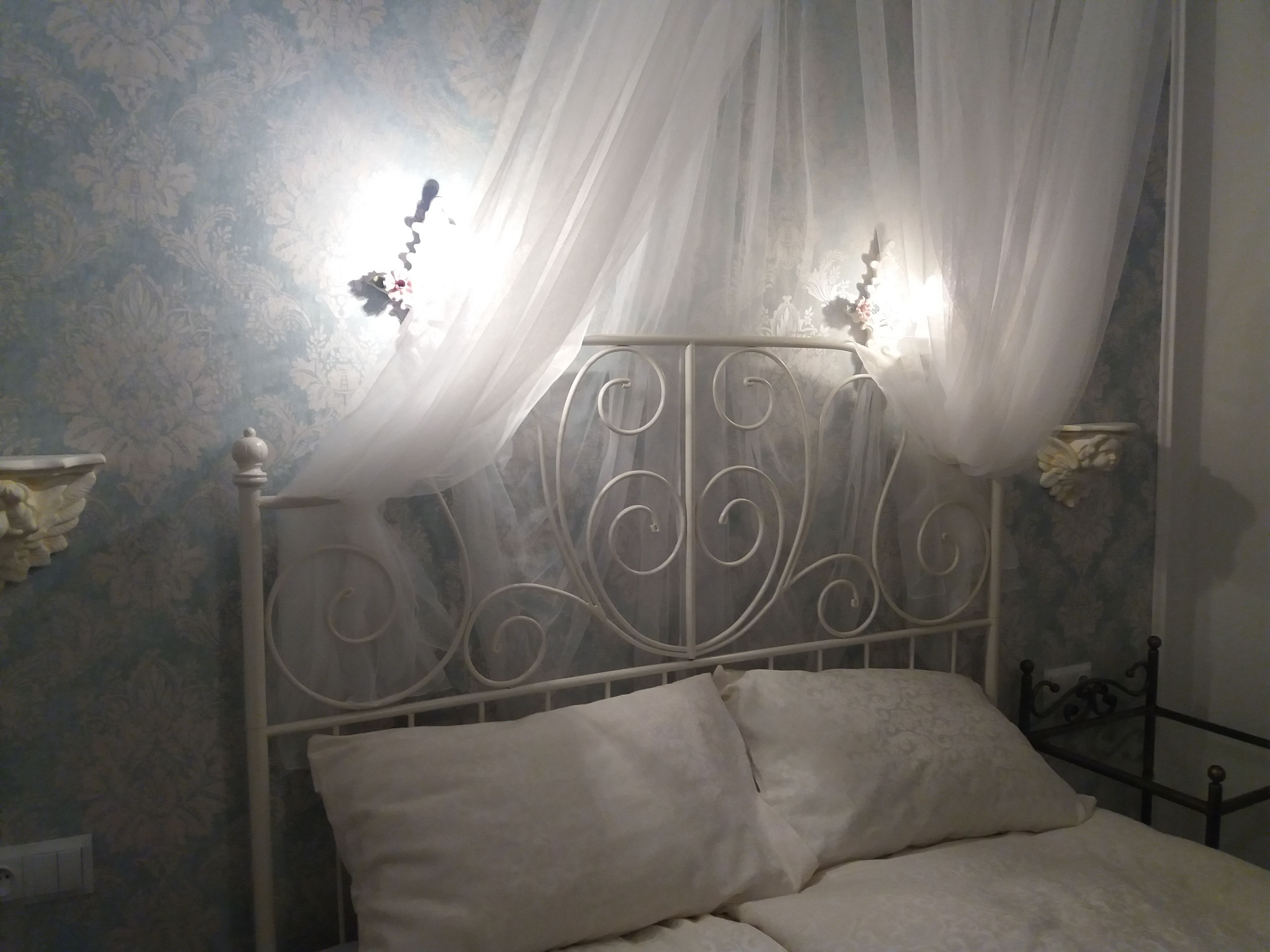 Una cama con dosel, un cabecero de metal decorativo y apliques de pared.