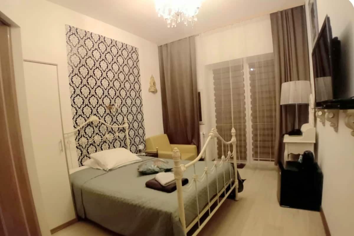 A bedroom with a bed, a chair, a TV, and a window with curtains.