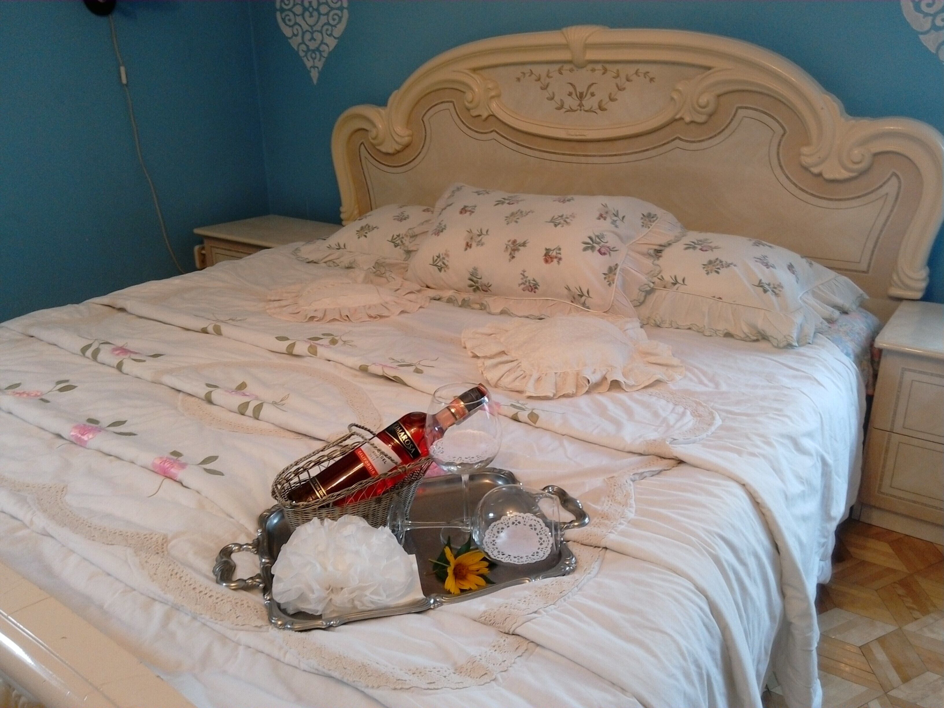 Un lit bien fait, avec une literie à motifs floraux, un plateau avec une bouteille et un objet décoratif posé sur le lit.