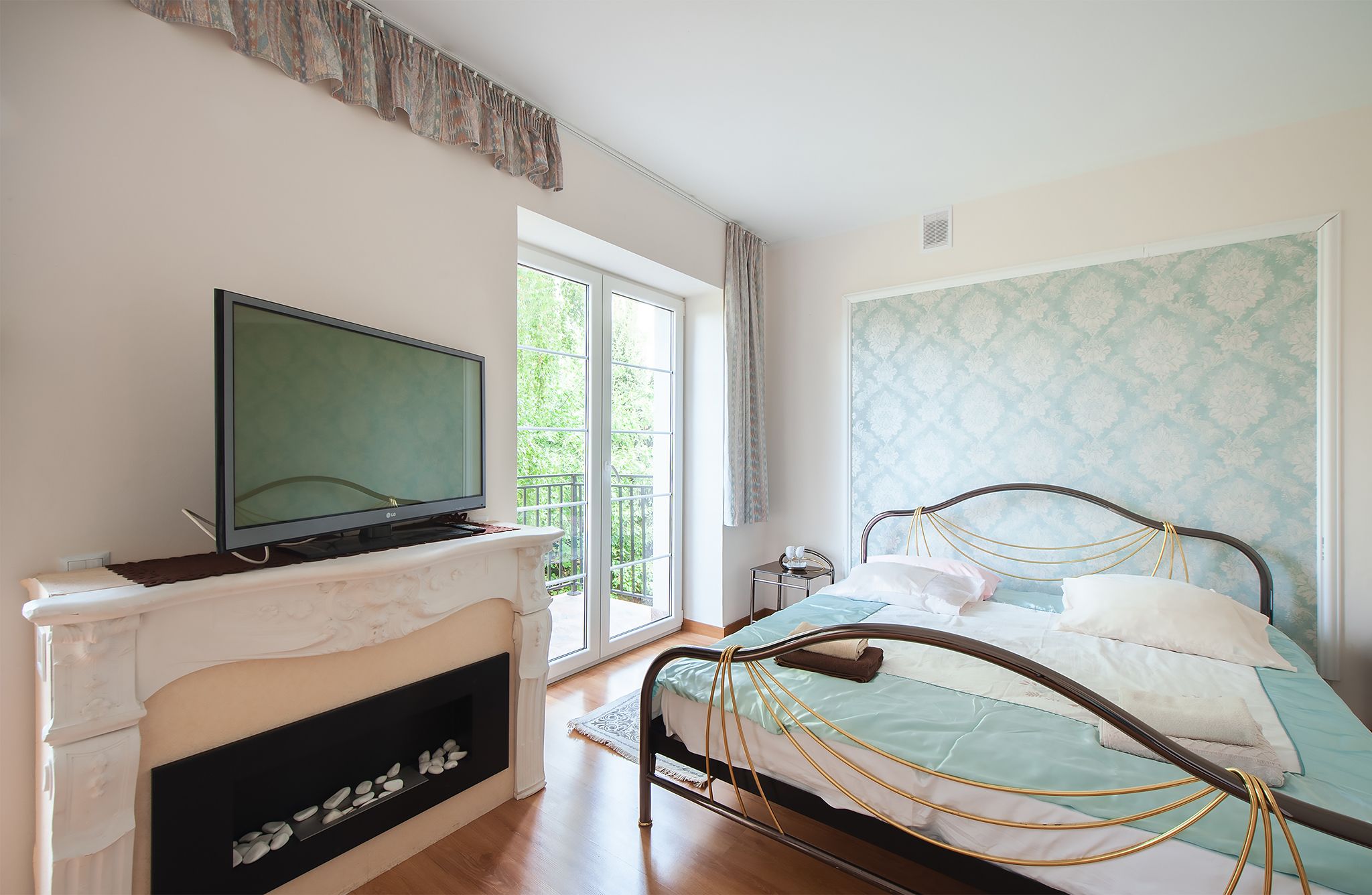Ein Schlafzimmer mit Fernseher auf einem Kamin, einem Bett mit Kopfteil und einem Fenster mit Blick auf Grünflächen.