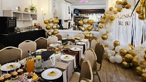 Comedor con mesas dispuestas para una comida, zona de bar y un arco decorado con globos.