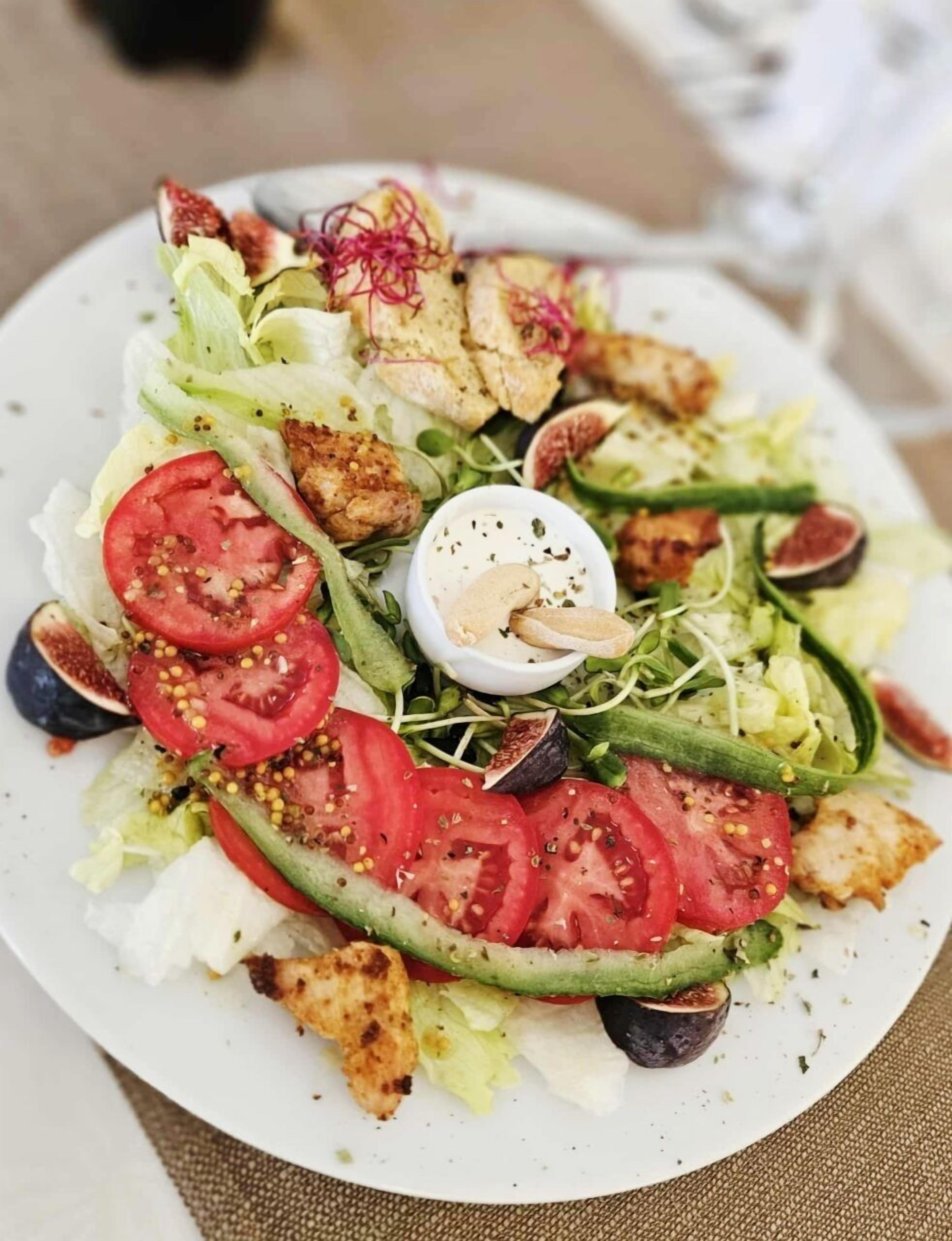 A plate of mixed greens salad with tomatoes, cucumbers, and grilled chicken pieces.