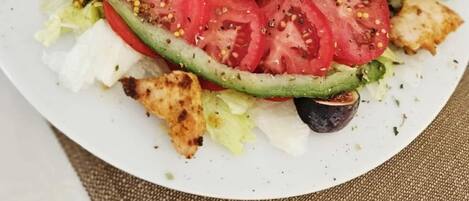 A plate of mixed greens salad with tomatoes, cucumbers, and grilled chicken pieces.
