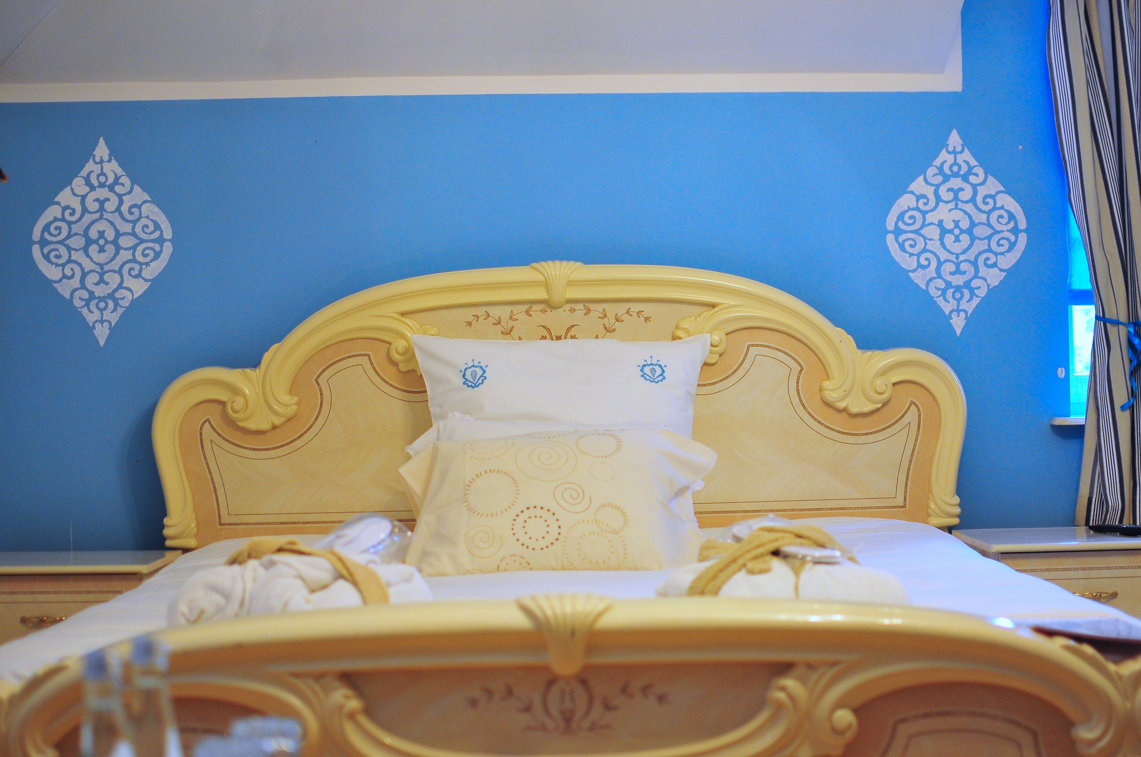 Un lit doté d’une tête de lit décorative, d’un oreiller blanc orné d’un motif circulaire et d’un mur bleu agrémenté de motifs en forme de losanges.