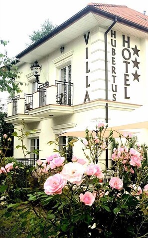 A two-story villa with a balcony, a sign reading "VILLA HUBERTUS HOTEL," and pink roses in the foreground. - Hotel Villa Hubertus Kutno (Kutno)