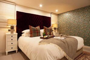 A neatly made bed with a plush headboard, two bedside tables with lamps, and a floral wallpaper. - The Dunstane - No 4 (Edinburgh)