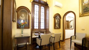 A dining area with a wooden table and chairs, a vase with flowers, and a stained glass window. - Guesthouse Borromeo Roma (Rome)