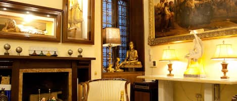 A room with a fireplace, a Buddha statue, a painting, and a table with a bottle and bowl.