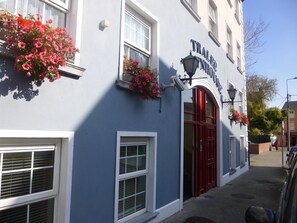 A building with a blue facade, a red door, and flower boxes on the windows.