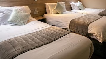 A hotel room with three beds arranged in a row, each with a headboard and pillows.