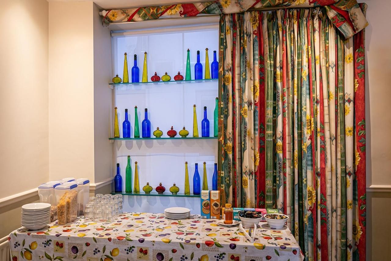 A dining area with a table set for guests, featuring a patterned tablecloth and a window with colorful curtains.