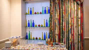 A dining area with a table set for guests, featuring a patterned tablecloth and a window with colorful curtains.