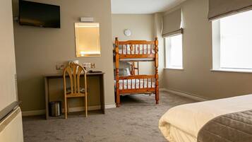 A hotel room with a bed, a desk with a chair, a television, a window, and a bunk bed.