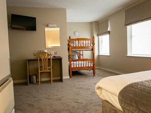 A hotel room with a bed, a desk with a chair, a television, a window, and a bunk bed.