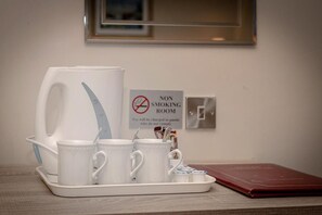 A tray with white mugs and a coffee maker, a non-smoking sign, and a red book on a table.