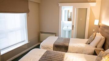 A hotel room with two beds, a window, a radiator, a sink, and a mirror.