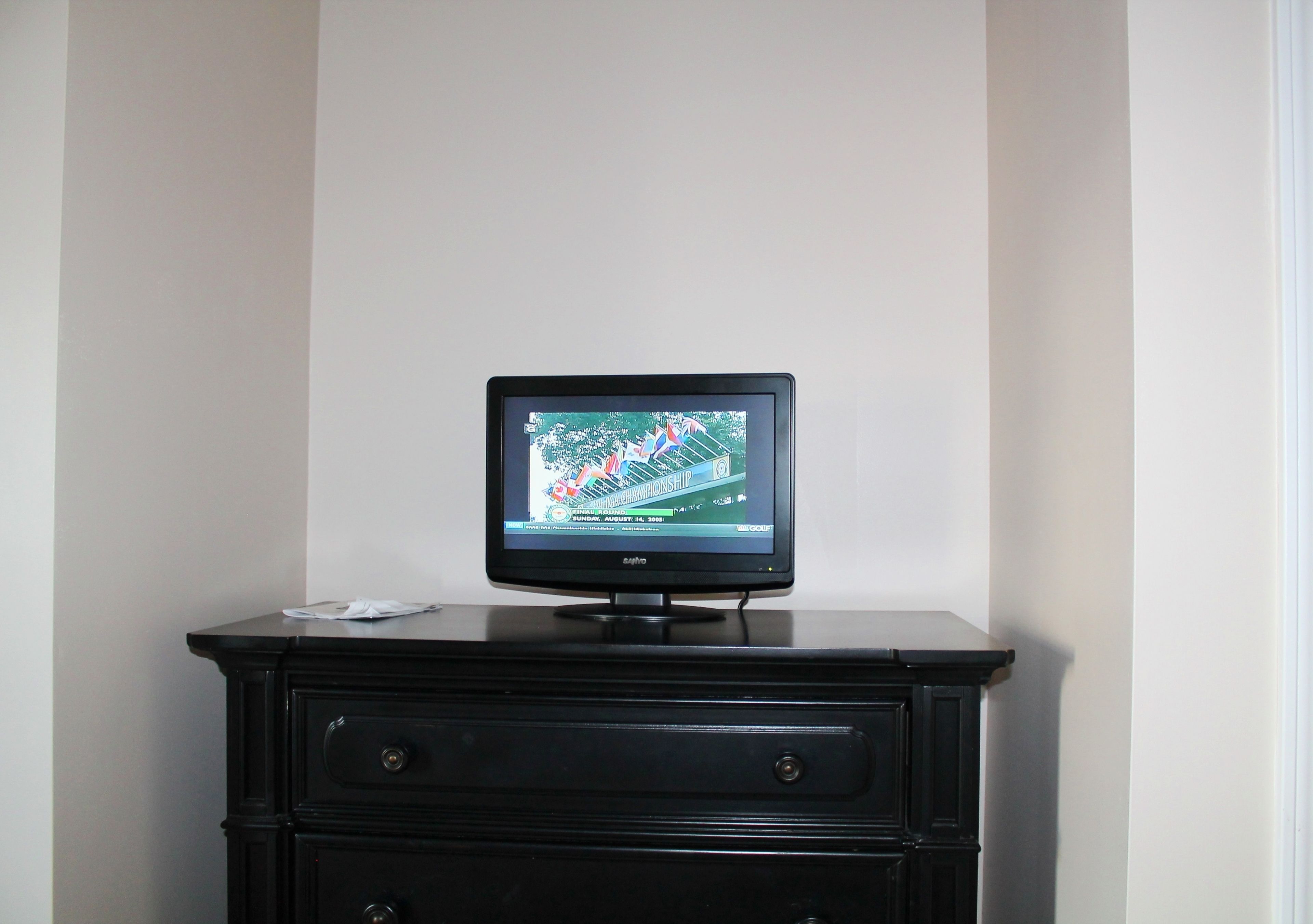 A television on a black dresser in a room with white walls.