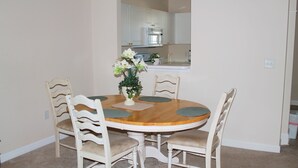 Een eetgedeelte met een ronde houten tafel, vier stoelen en een vaas met bloemen.