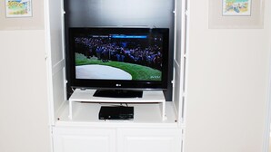Een televisie bevestigd aan een wit kastje, met een afstandsbediening eronder.