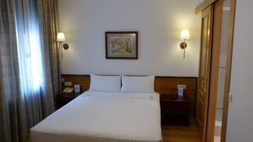 A hotel room with a large bed, two bedside tables, a ceiling fan, a painting on the wall, and a door to the right.
