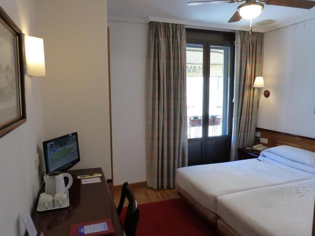 A hotel room with a bed, a desk with a computer, a coffee maker, and a chair.