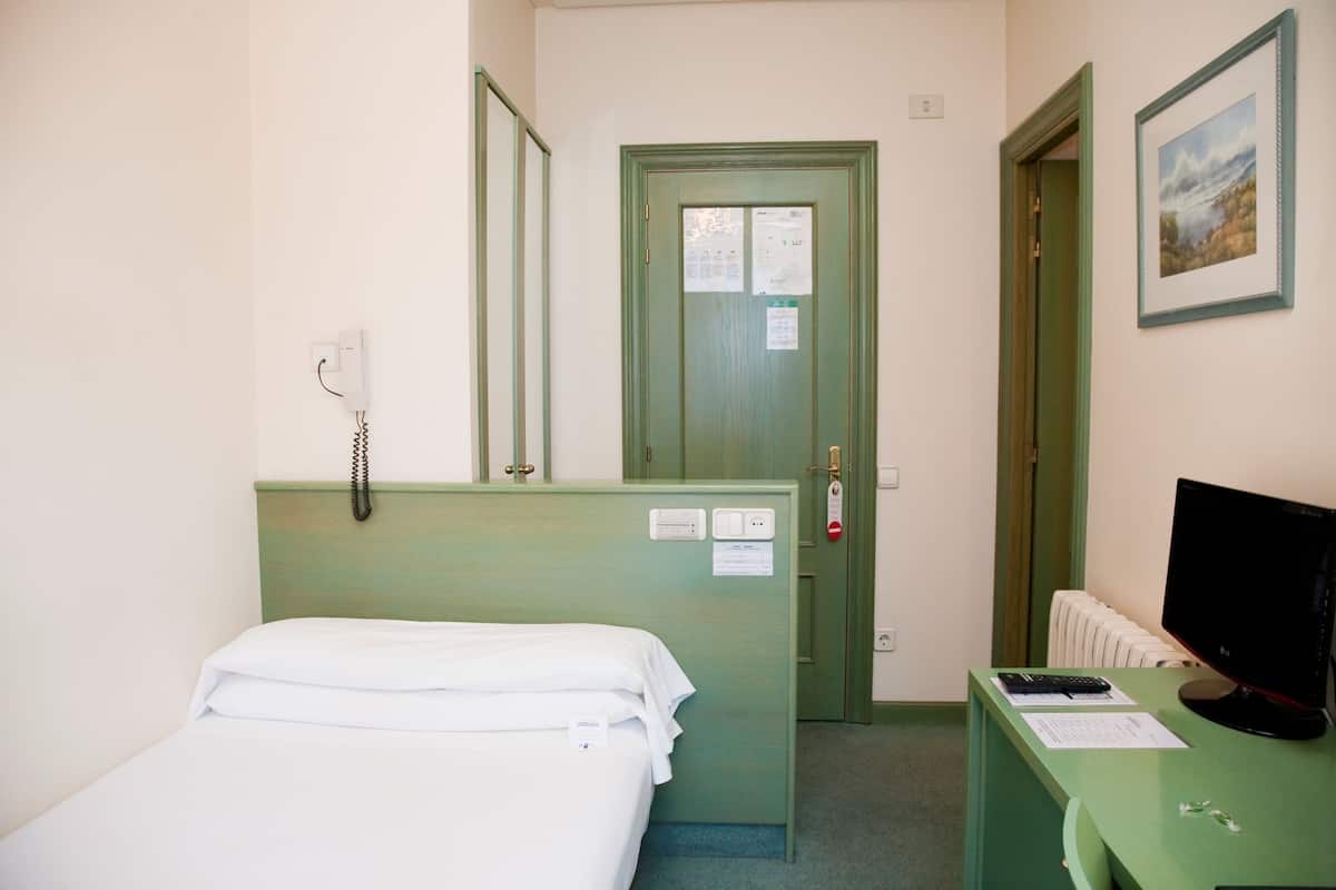 Une chambre d’hôtel équipée d’un lit, d’un bureau avec un ordinateur, d’un téléphone et d’une porte donnant sur l’extérieur.