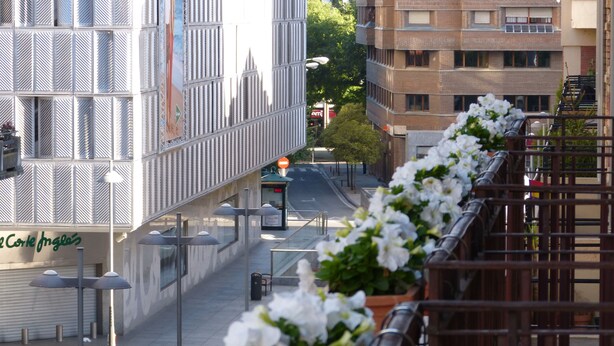En moderne bygning med metalbeklædning og en række hvide blomster i kasser langs altanrelingen.