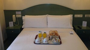Et hotelværelse med en seng, to sengeborde, et bakke med morgenmad og et billede på væggen.